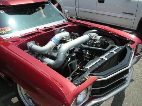 1998 Ford Crown Victoria - The engine bay of a red car features a complex turbocharger setup, with a white pickup truck visible behind it.