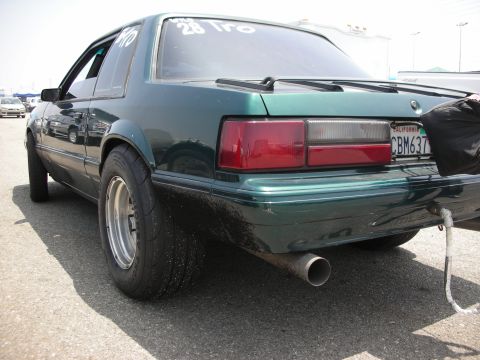 1998 Ford Crown Victoria - Green fox body Mustang with drag tires and visible roll cage, rear view.