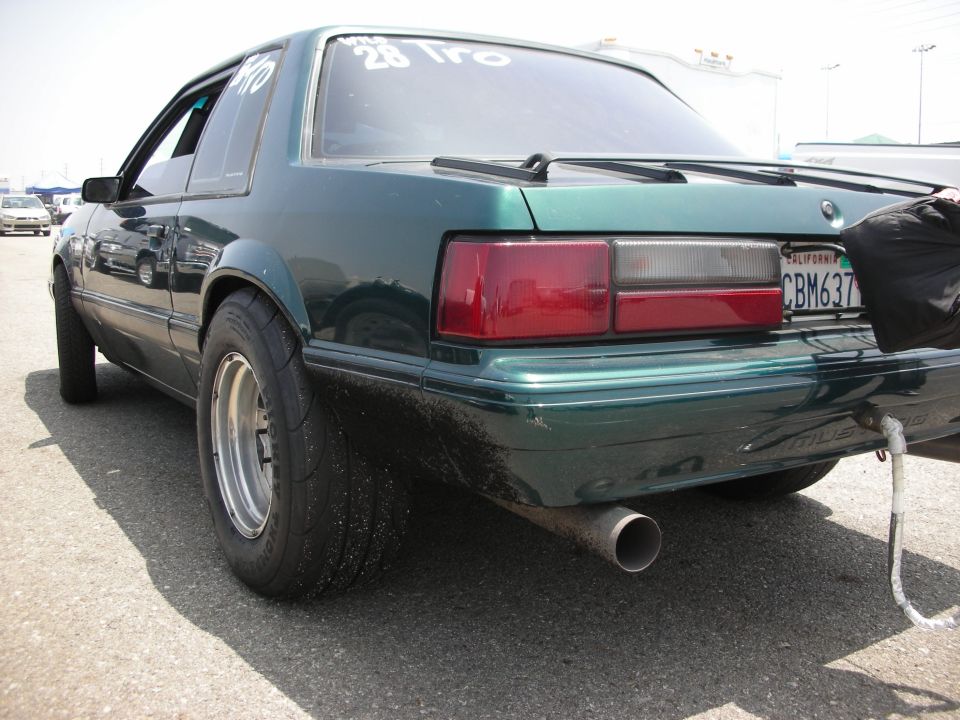 Rear view of a green fox body Mustang with drag slicks and a roll cage visible through the window. Text on the rear window reads '28 Tro'