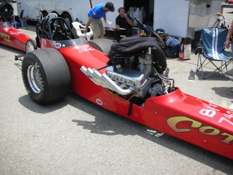 1998 Ford Crown Victoria - A dragster sits on asphalt with a trailer and people in the background.