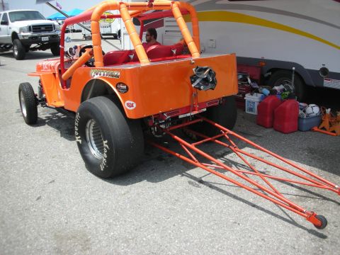 1998 Ford Crown Victoria - An orange dragster is parked next to a trailer with various items including gas cans and tools.