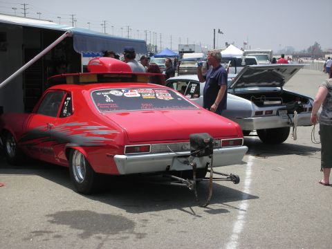 1998 Ford Crown Victoria - A red drag car is parked next to a silver car with its trunk open at a race track.