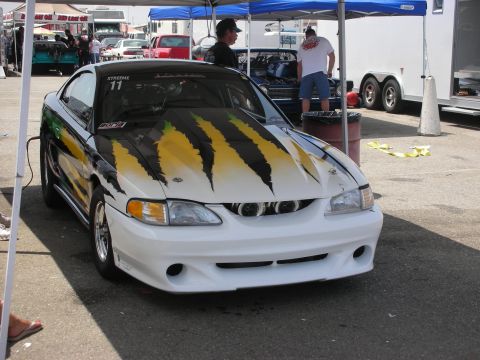 1998 Ford Crown Victoria - A modified Ford Mustang with custom paint and bodywork sits under a tent at an outdoor event.