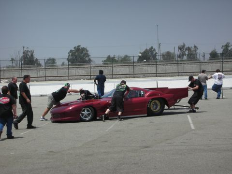 1998 Ford Crown Victoria - Crew members push a red drag car with an exposed engine on a track.