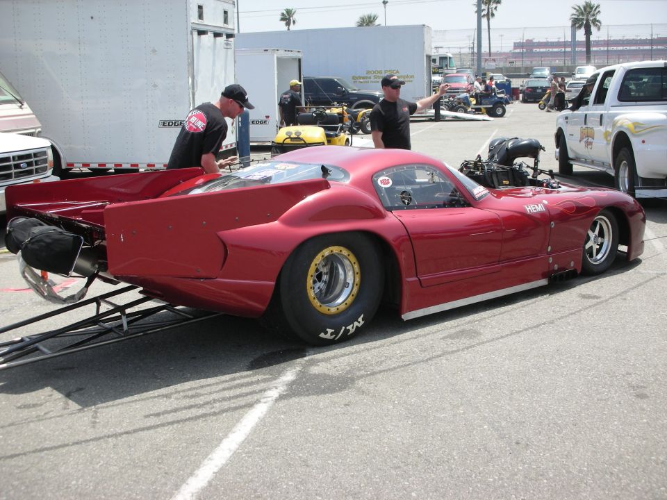 Red drag car with large rear tires and exposed engine, parked on asphalt