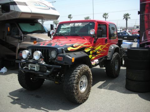 1998 Ford Crown Victoria - Modified red Jeep Wrangler with flame decals parked next to an RV and tires.