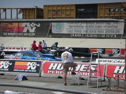 1998 Ford Crown Victoria - Drag cars are staged at the starting line with spectators and advertising banners in the background.