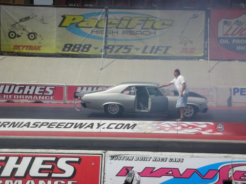 1998 Ford Crown Victoria - A man stands next to a silver coupe on a drag strip, with smoke coming from the rear tires.