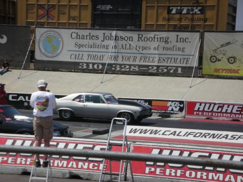1998 Ford Crown Victoria - A silver drag car sits on the track next to a black car, with a Hughes Performance banner in the background.