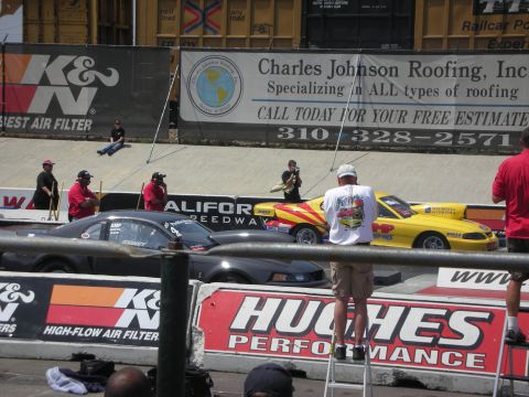 1998 Ford Crown Victoria - Drag racing cars line up at the starting line, with spectators and advertising banners in the background.