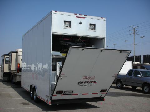 1998 Ford Crown Victoria - A trailer is parked with its ramp down, revealing a vehicle within, while other vehicles and trailers are visible in the background.