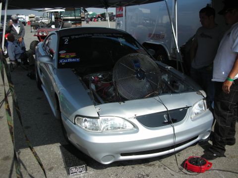 1998 Ford Crown Victoria - A silver Ford Mustang Cobra sits with its hood open, revealing a large fan in the engine bay.