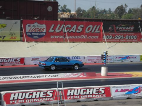 1998 Ford Crown Victoria - A blue coupe races down the drag strip, with various sponsor banners visible in the background.