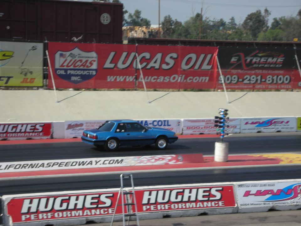 Blue coupe drag racing down a track with Lucas Oil banners in the background