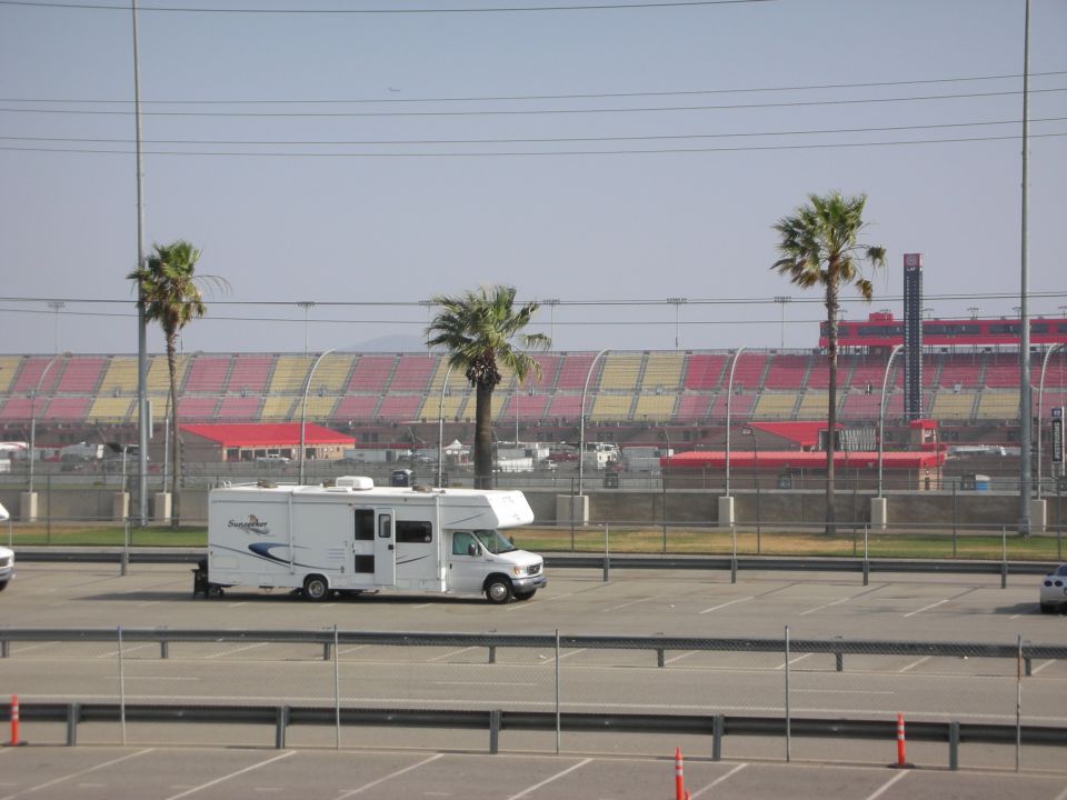 White RV parked in a lot with stadium seating in the background