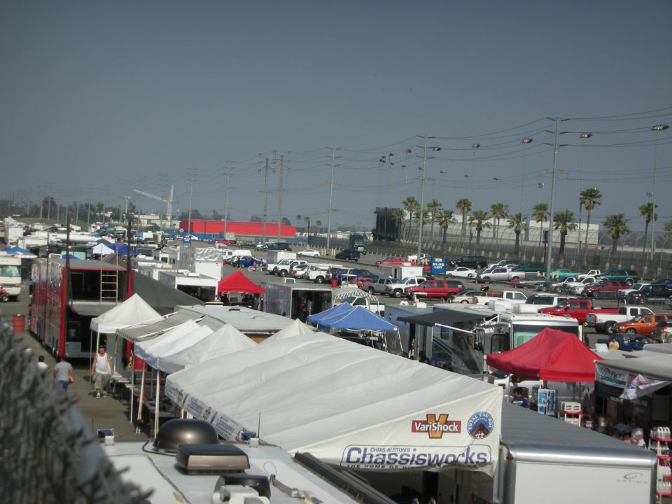 Many cars, trucks, RVs, and tents are parked in a large lot under a hazy sky