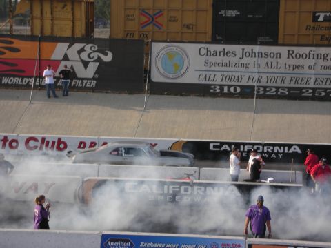 1998 Ford Crown Victoria - A silver drag racing car is seen on the track at California Speedway, surrounded by smoke.