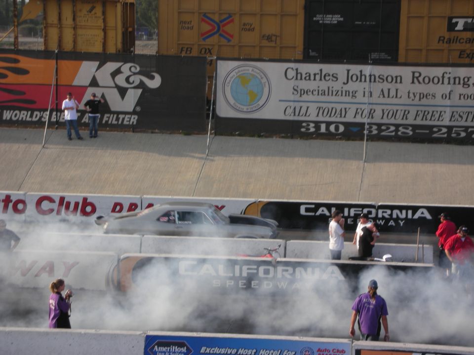 Silver drag car on track with smoke, California Speedway signage