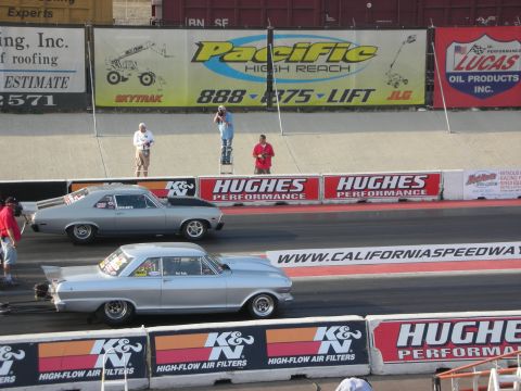 1998 Ford Crown Victoria - Two drag cars compete on a sunny day at a speedway with sponsor banners in the background.