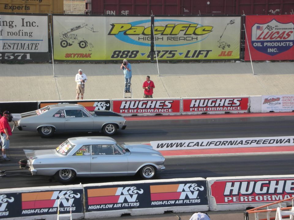 Two silver drag cars on a race track, one in front of the other. Both have racing modifications