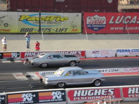 1998 Ford Crown Victoria - Two classic silver drag cars compete on a race track, with sponsor banners visible in the background.