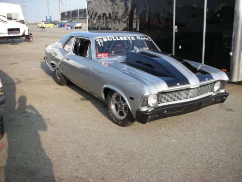 1998 Ford Crown Victoria - This silver 1969 Chevrolet Nova drag car features a prominent black hood scoop and racing decals, parked next to a trailer.