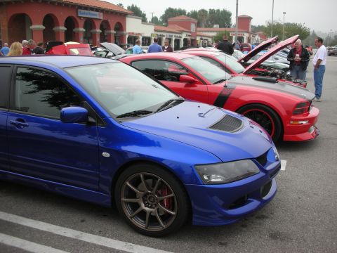 1998 Ford Crown Victoria - A blue Mitsubishi Lancer Evolution is parked in a lot with other cars, including a red Ford Mustang.