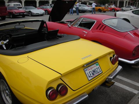 1998 Ford Crown Victoria - A yellow convertible sports car is parked next to a red coupe at a car meet.