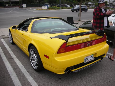 1998 Ford Crown Victoria - A bright yellow sports car is parked at an angle, showing its rear end with a prominent black spoiler and a custom license plate.