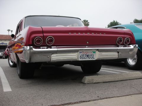 1998 Ford Crown Victoria - A red 1964 Chevrolet sedan is parked next to another vehicle, showing its rear end with distinctive taillights and a chrome bumper.