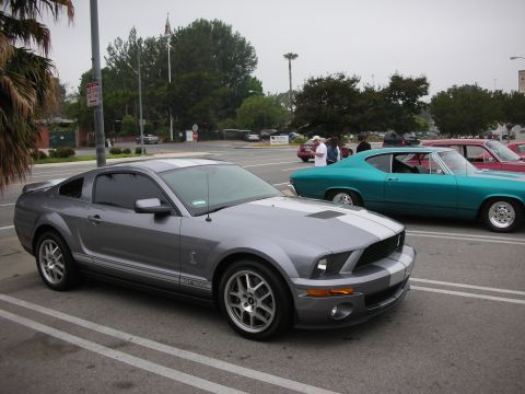 1998 Ford Crown Victoria - A modern Ford Mustang Shelby GT500 is parked in a lot next to a vintage teal coupe and a red car.