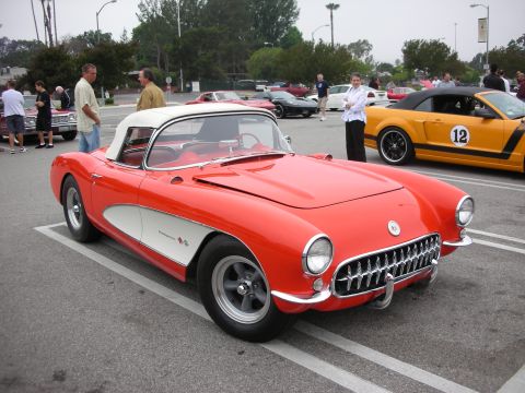 1998 Ford Crown Victoria - A classic red and white Chevrolet Corvette is parked at a car meet, with other vehicles visible in the background.