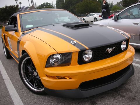 1998 Ford Crown Victoria - A yellow Ford Mustang Boss 302 is parked in a lot, with another car visible to its right.