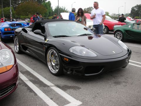 1998 Ford Crown Victoria - A black convertible sports car is parked at an outdoor car meet, with other vehicles in the background.