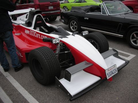 1998 Ford Crown Victoria - A red and white open-wheel race car is parked in a lot with other vehicles visible in the background.