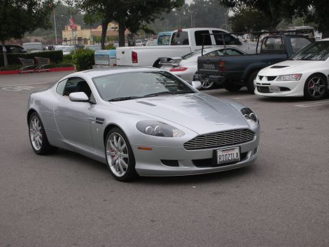 1998 Ford Crown Victoria - A silver Aston Martin coupe is parked in a lot, with other vehicles visible in the background.