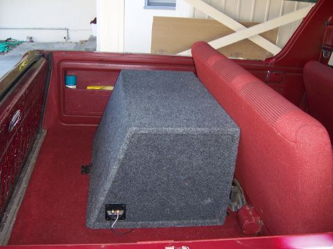 1991 Ford Bronco - The interior of a vehicle shows a large subwoofer box behind the red seats.