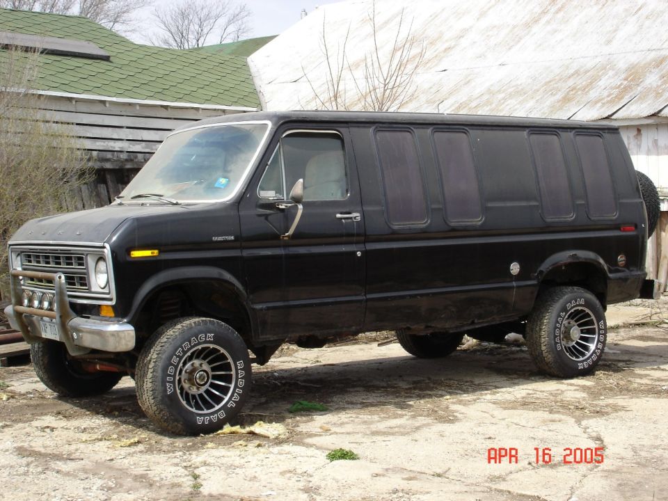 Black van with custom wheels and a brush guard, parked on dirt