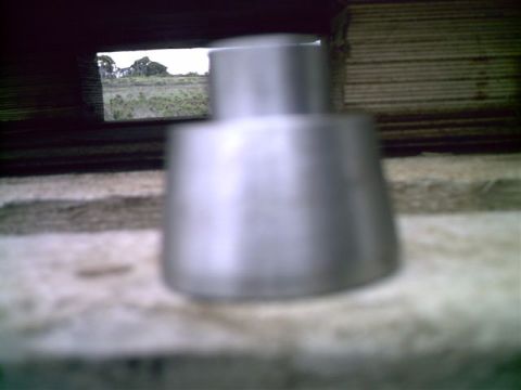 1964 Ford 427 - A close-up of a metal exhaust tip is visible, with a rural landscape seen through a dark opening in the background.