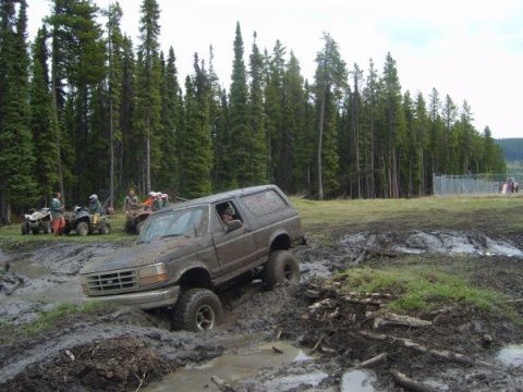 1995 Ford Bronco - Ford Bronco navigating a muddy off-road course with ATVs nearby.
