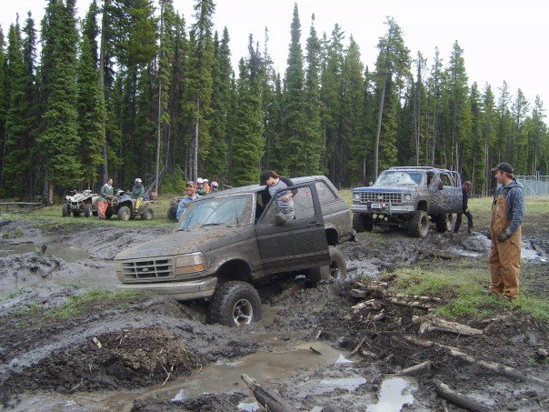 Ford Bronco and Chevy SUV stuck in mud pit with ATVs nearby