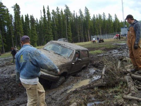 1995 Ford Bronco - Off-road vehicle stuck deep in mud with onlookers nearby.