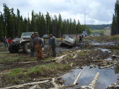 1995 Ford Bronco - Several off-road vehicles and people are gathered in a muddy field, with one truck stuck in the mire.