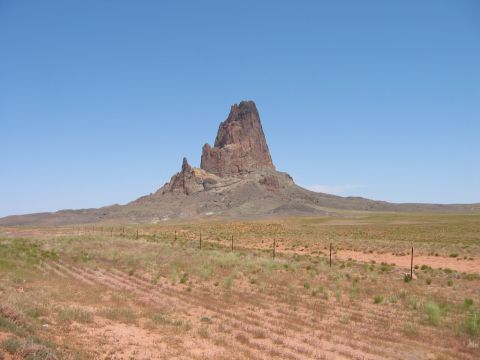 1997 Ford Ranger - A vast desert scene features a towering rock formation against a clear blue sky, with dry grass and a fence in the foreground.