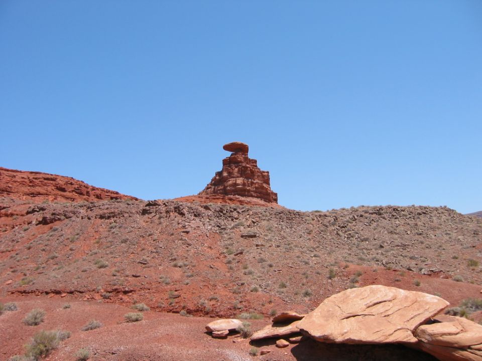 Desert landscape with red rock formations and a clear blue sky. Watermark reads SUPERMOTORS