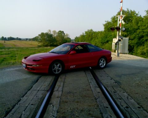 1993 Ford Probe - A red 1993 Ford Probe GT is positioned on railroad tracks with a crossing signal in the background.
