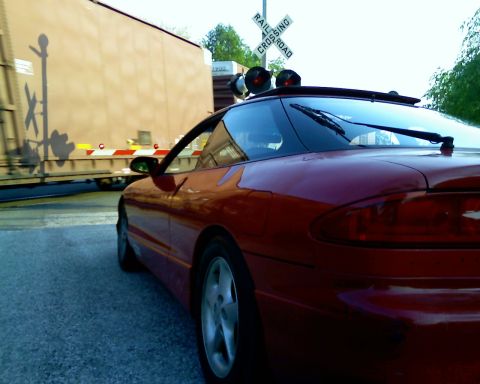 1993 Ford Probe - A red coupe waits at a railroad crossing as a train passes by.