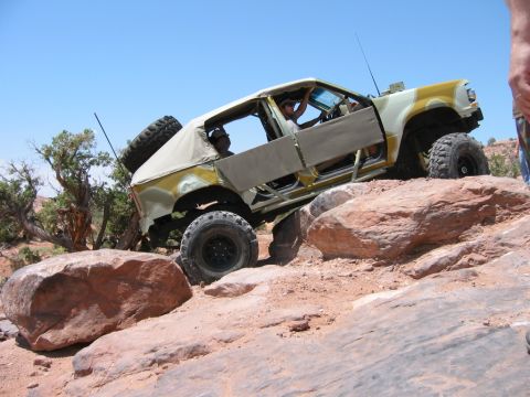 1997 Ford Ranger - This modified off-road vehicle is carefully maneuvering over large rocks on a sunny day.