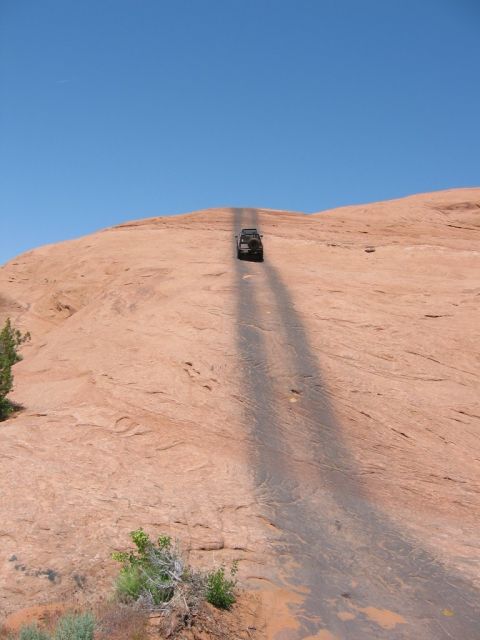 1997 Ford Ranger - A vehicle ascends a large rock formation on a sunny day, leaving tire tracks behind.