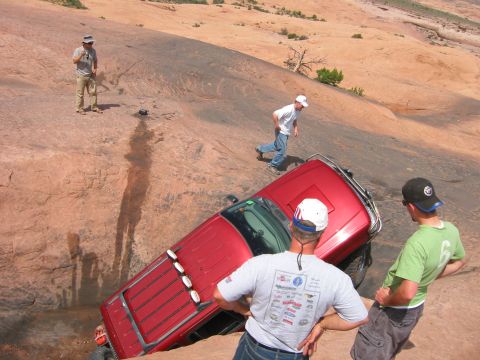 1997 Ford Ranger - A red 1997 Ford Ranger is stuck on a steep, rocky terrain in Moab, Utah, with onlookers assessing the situation.